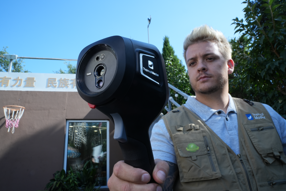 Person using a Thermal Master handheld thermal camera for an outdoor building inspection.