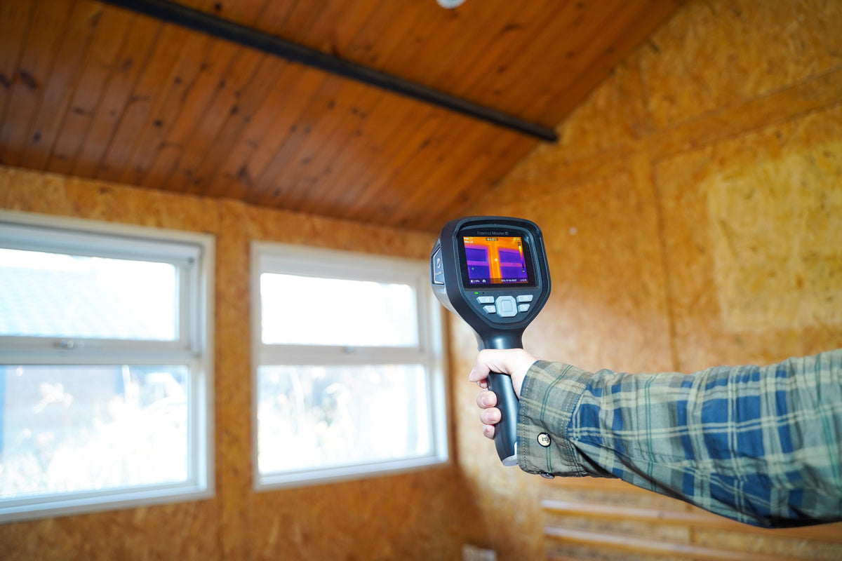 Thermal Master handheld thermal camera scanning walls and windows for heat loss during a home inspection.