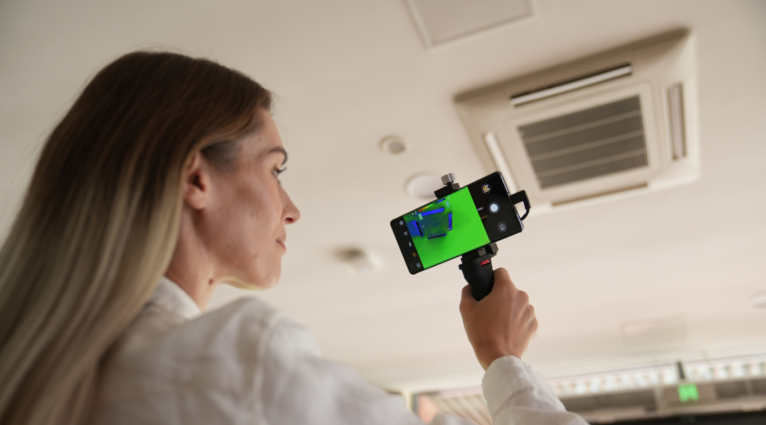 A woman uses her mobile phone thermal imaging camera to inspect an air conditioner.