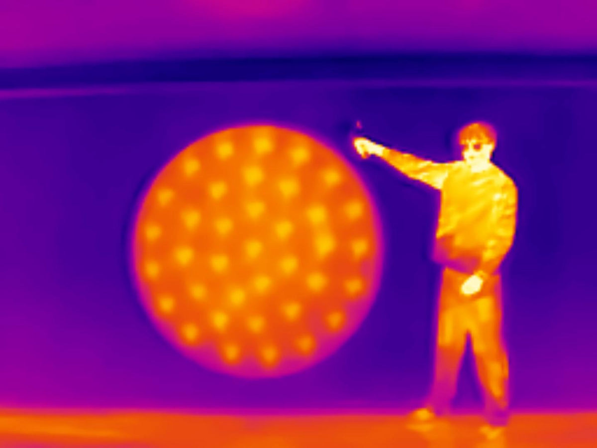 Thermal view of a person beside a large circular structure showing temperature differences.