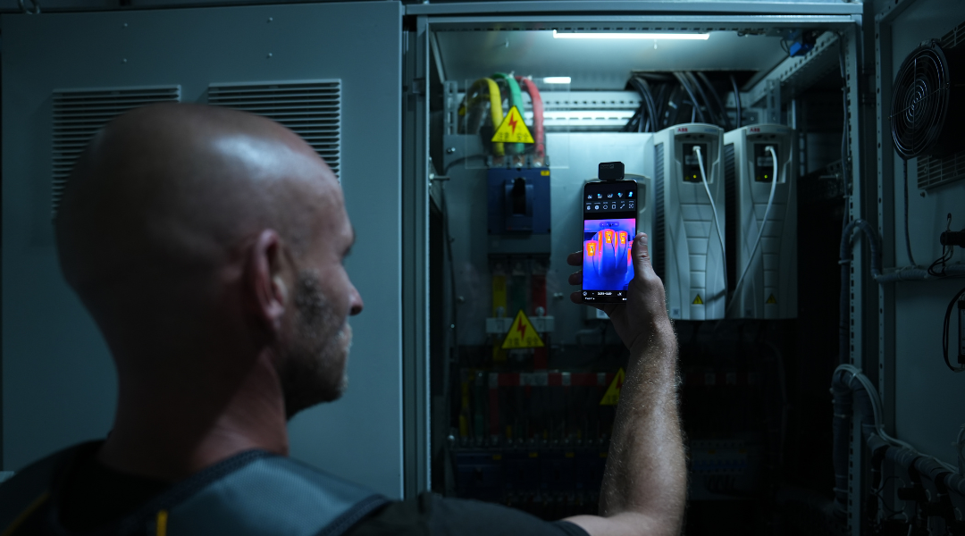 A man uses a thermal imager to inspect an electrical box.